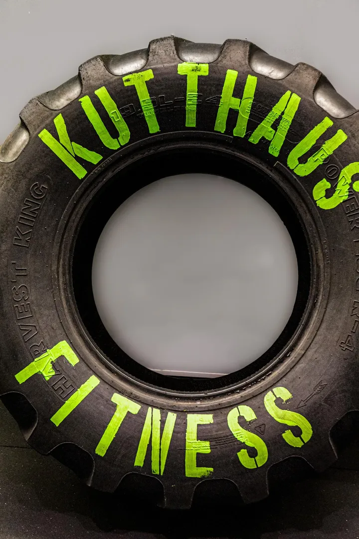 Tractor tire hand-painted with Kutthaus Fitness in bright green, standing on the gym floor